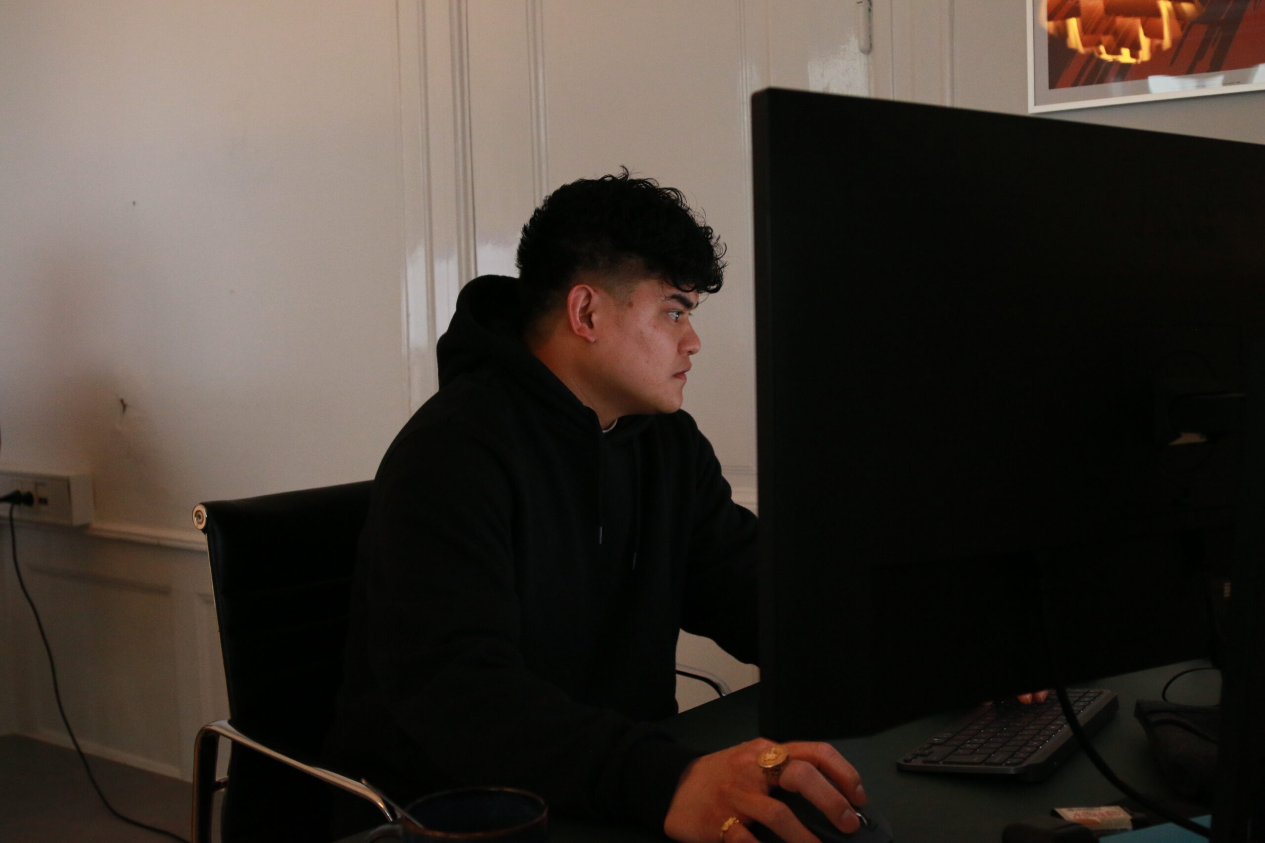 Person i sort hættetrøje arbejder ved en stor computerskærm på et kontor