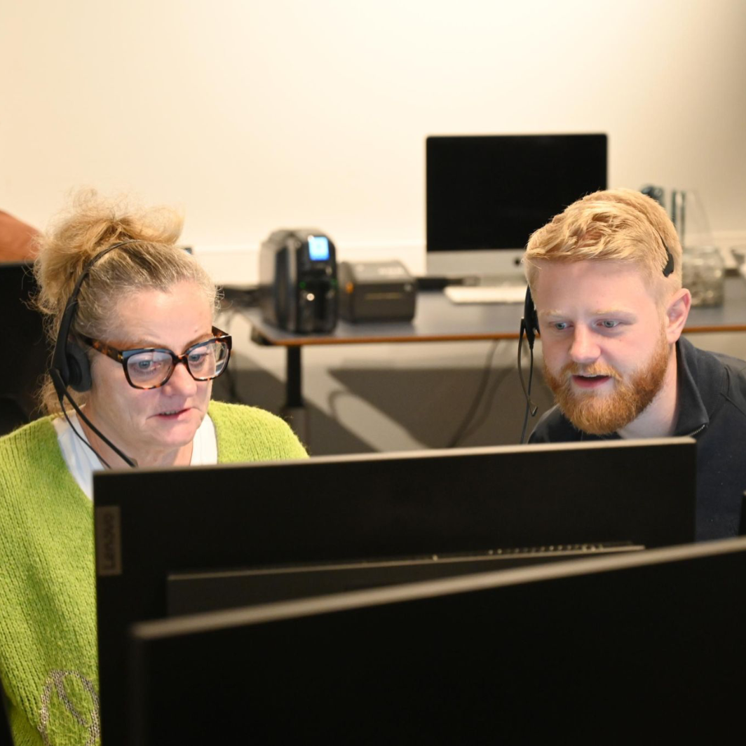 To kolleger med headset kigger sammen på en computerskærm i et kontor